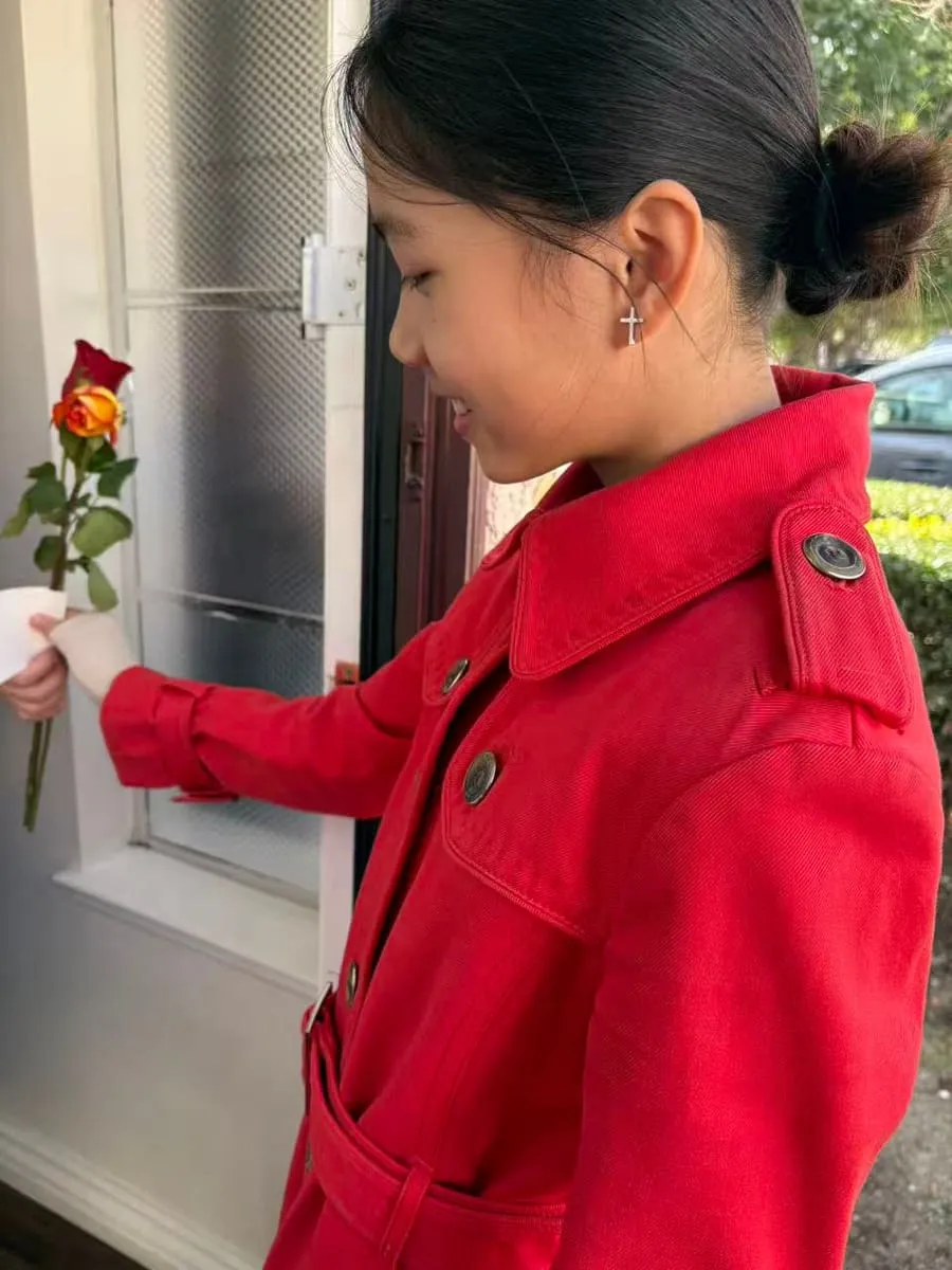 A girl in a red coat holds a single rose.