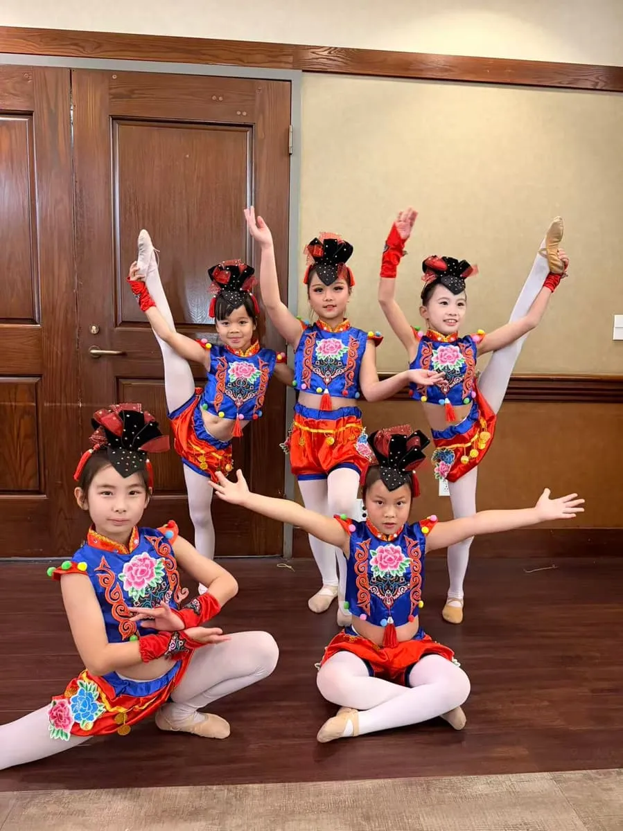 Five young dancers in embroidered costumes pose on the floor.