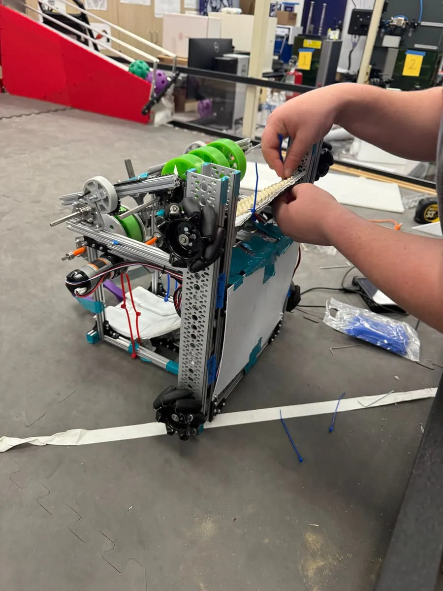 A student adjusts a robot’s intake on the practice field.