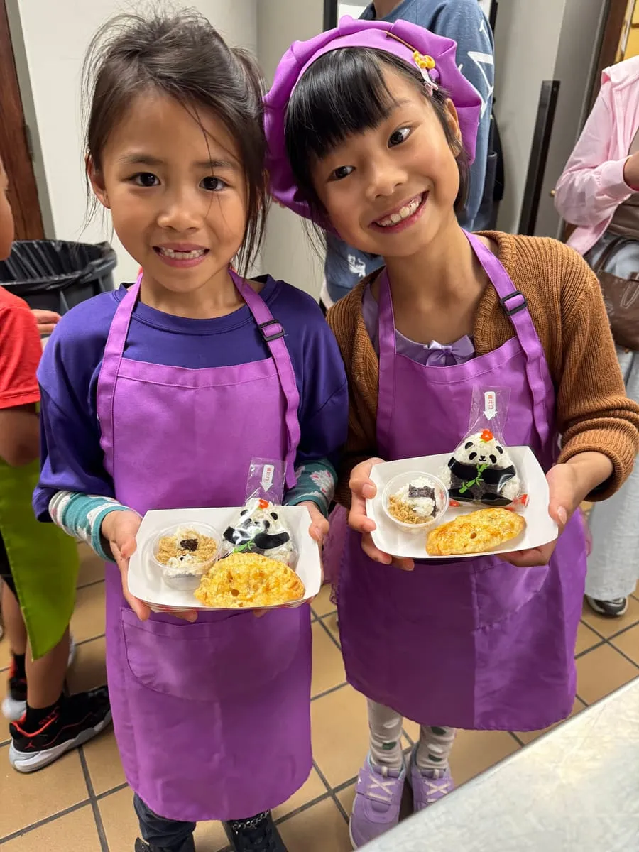 Two girls in purple aprons show their plates of food.
