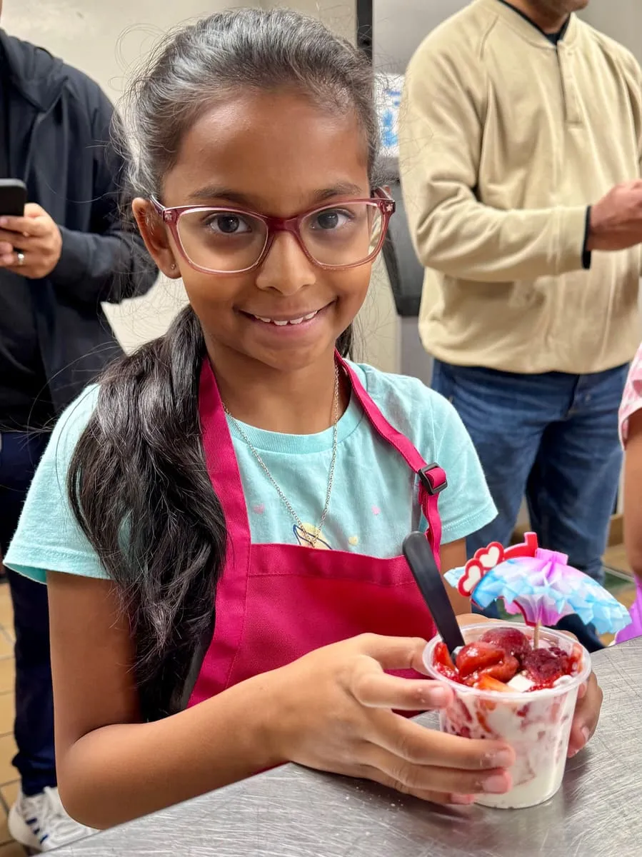 A girl in glasses holds a fruit dessert cup she made.