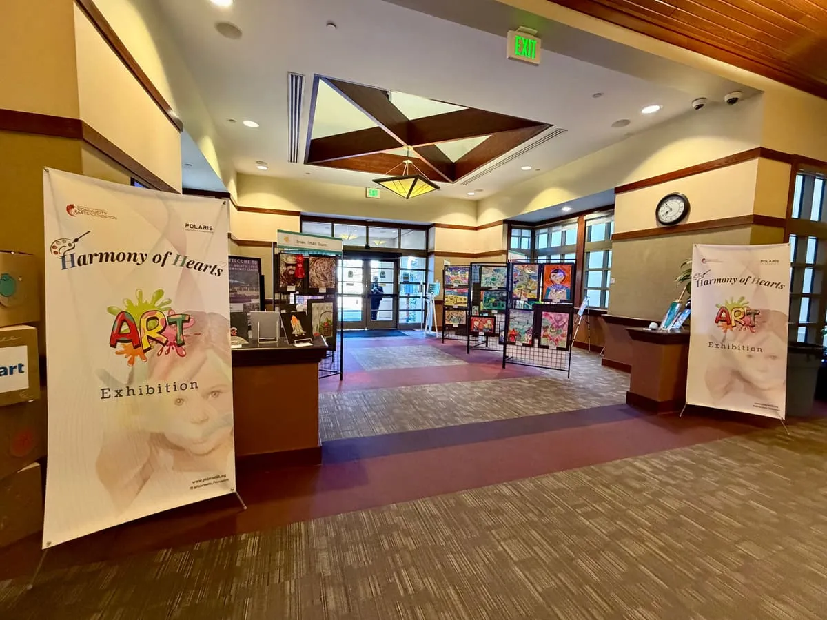Harmony of Hearts banners frame the community center lobby, with art panels set out across the floor.