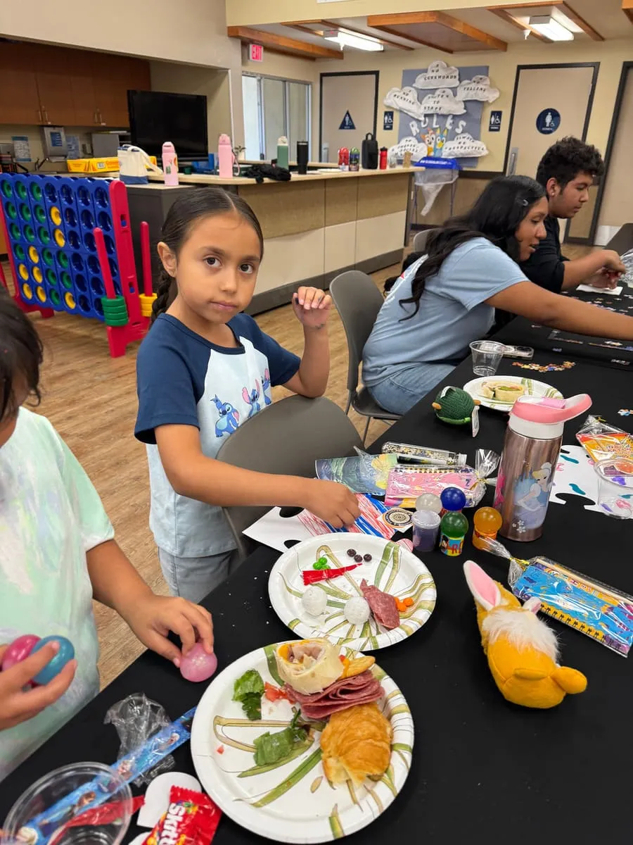 A girl sits at a table with the plates of food she has prepared.