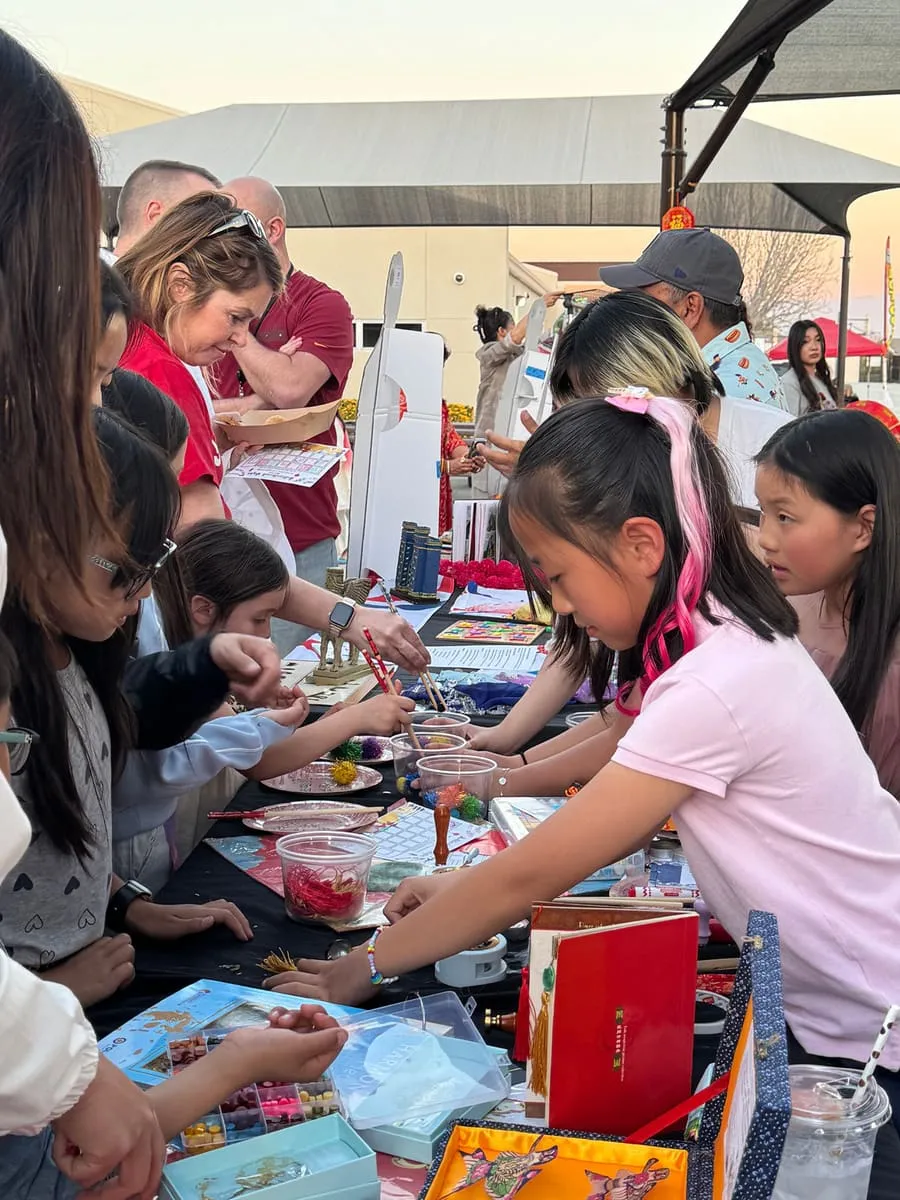 Children crowd a craft table at an evening festival.