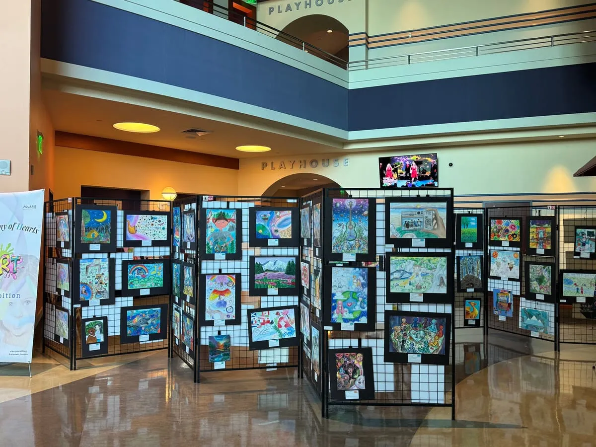 Rows of black panels covered in student artwork fill a large hall under a balcony.