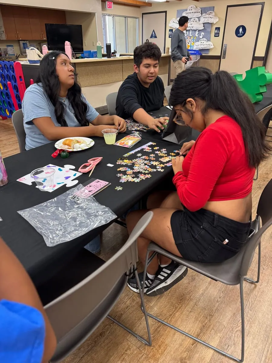 Teenagers work on puzzles together at a long table.