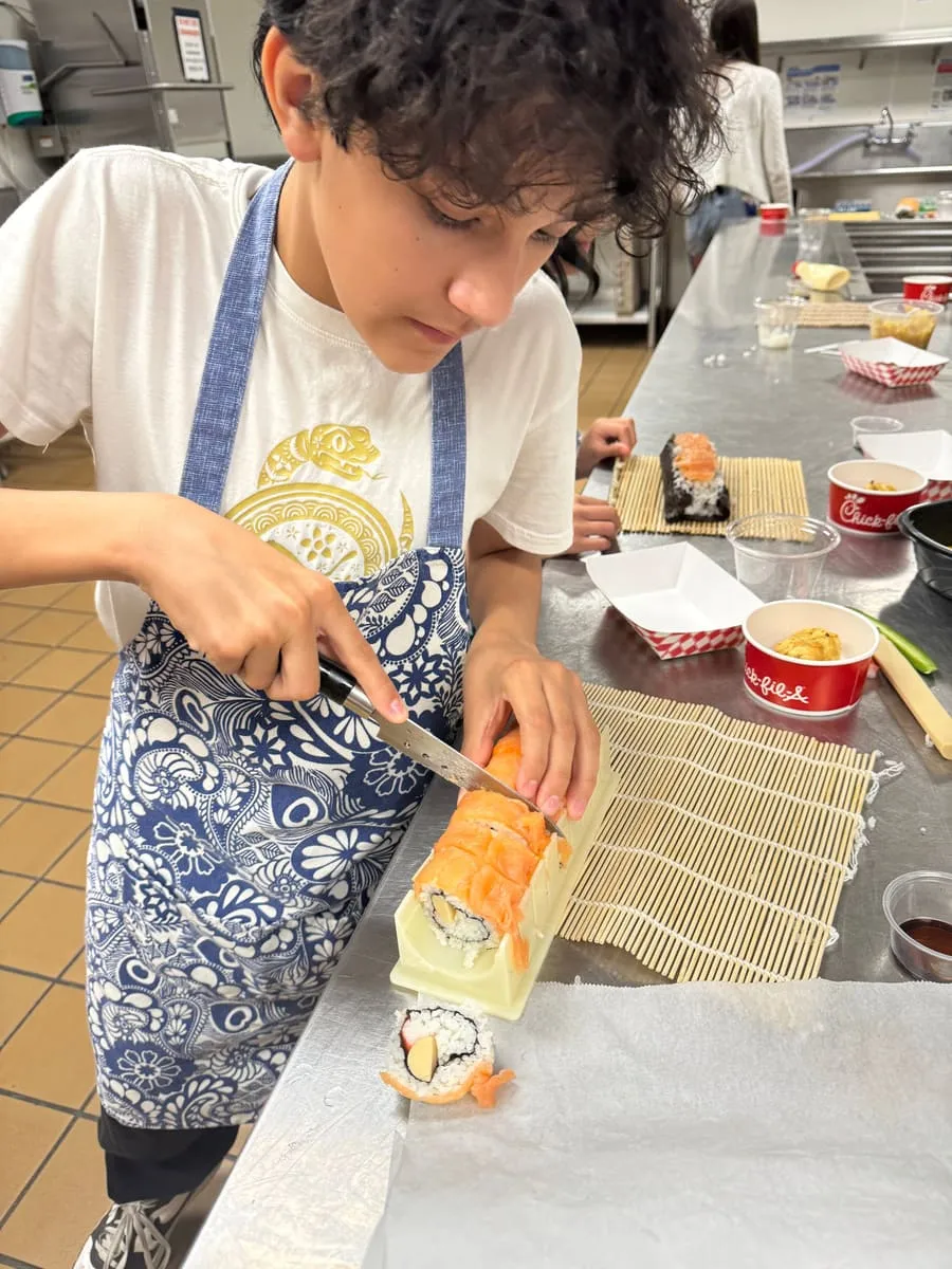 A boy rolls sushi on a bamboo mat.