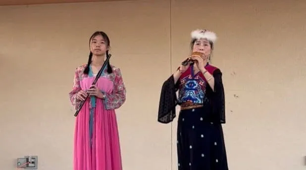 Two performers in traditional dress; one plays a flute.