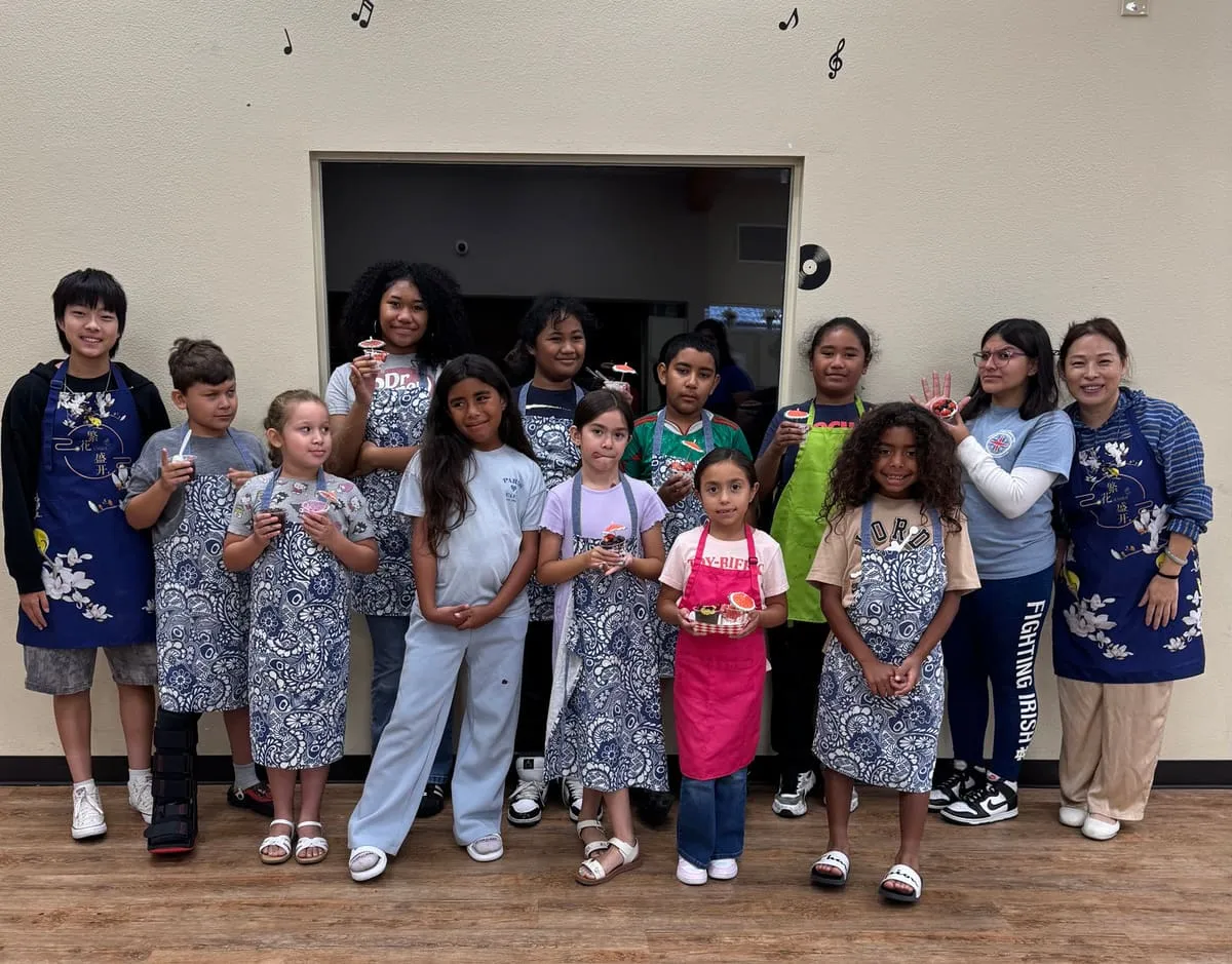 A cooking class group in aprons poses with their instructors.