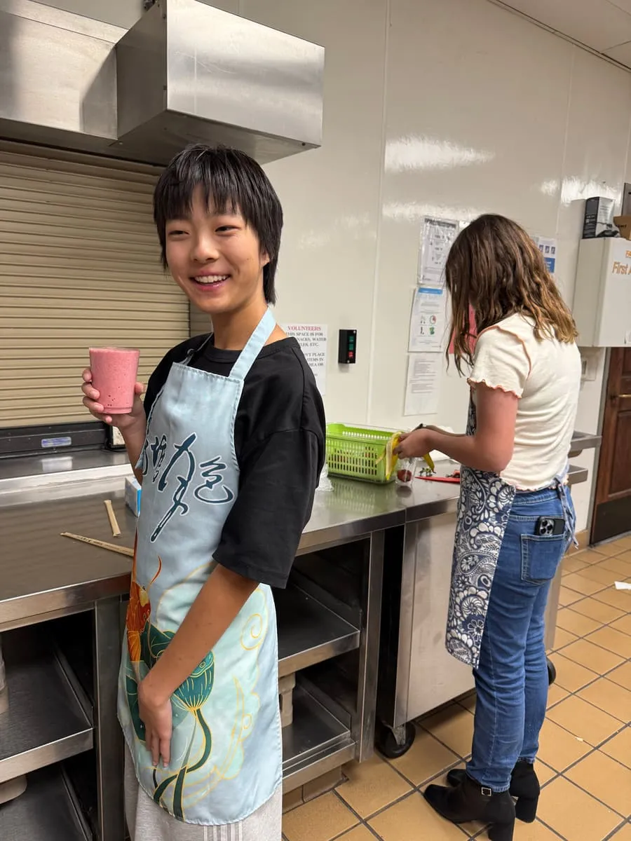 A boy in a printed apron smiles in the kitchen.
