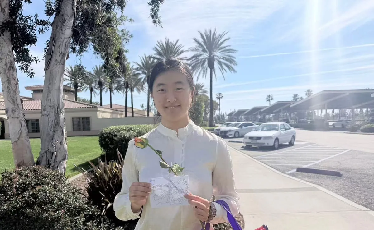 A young woman outdoors holds a rose and a card.
