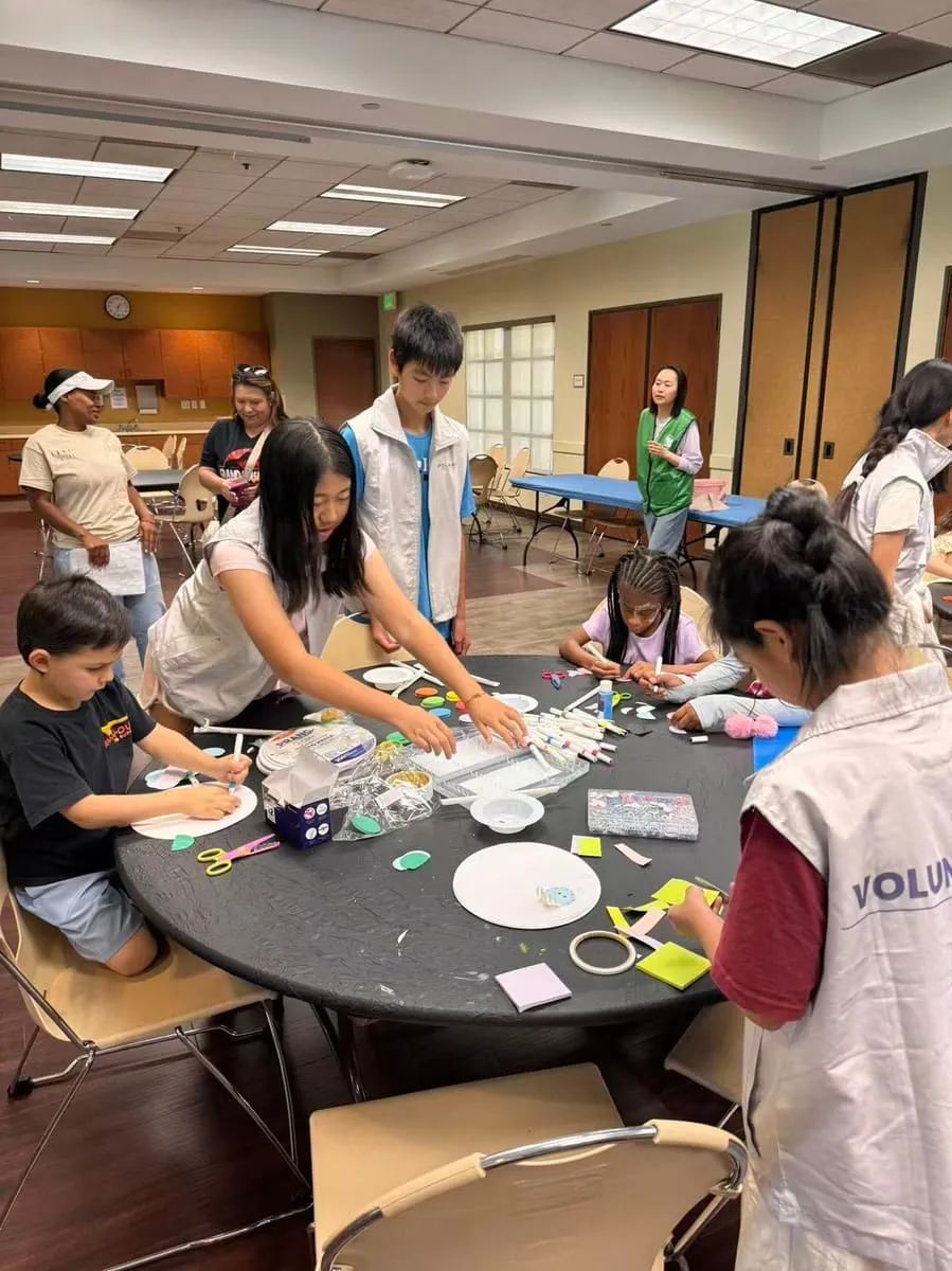 Children and volunteers make crafts around a round table.