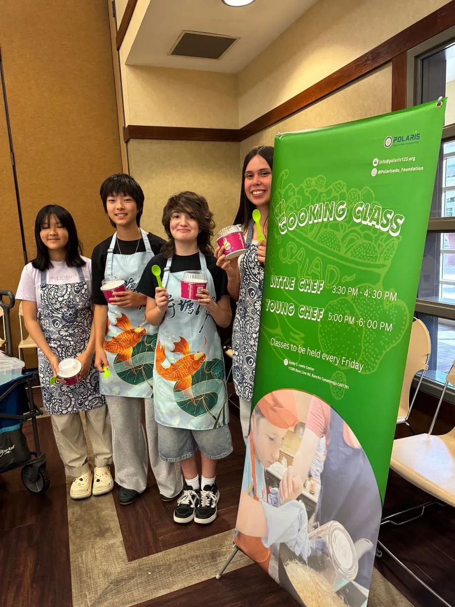 Students in aprons hold their desserts next to the Cooking Class banner.