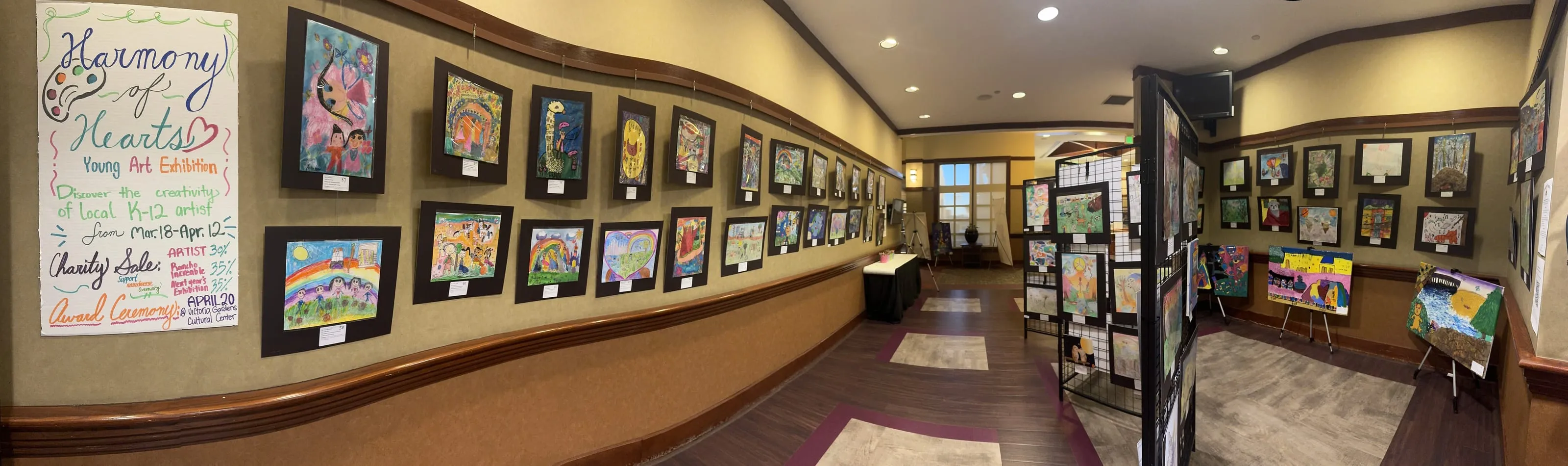 Panorama of the exhibition hall with framed artwork on every wall and display panels down the middle.