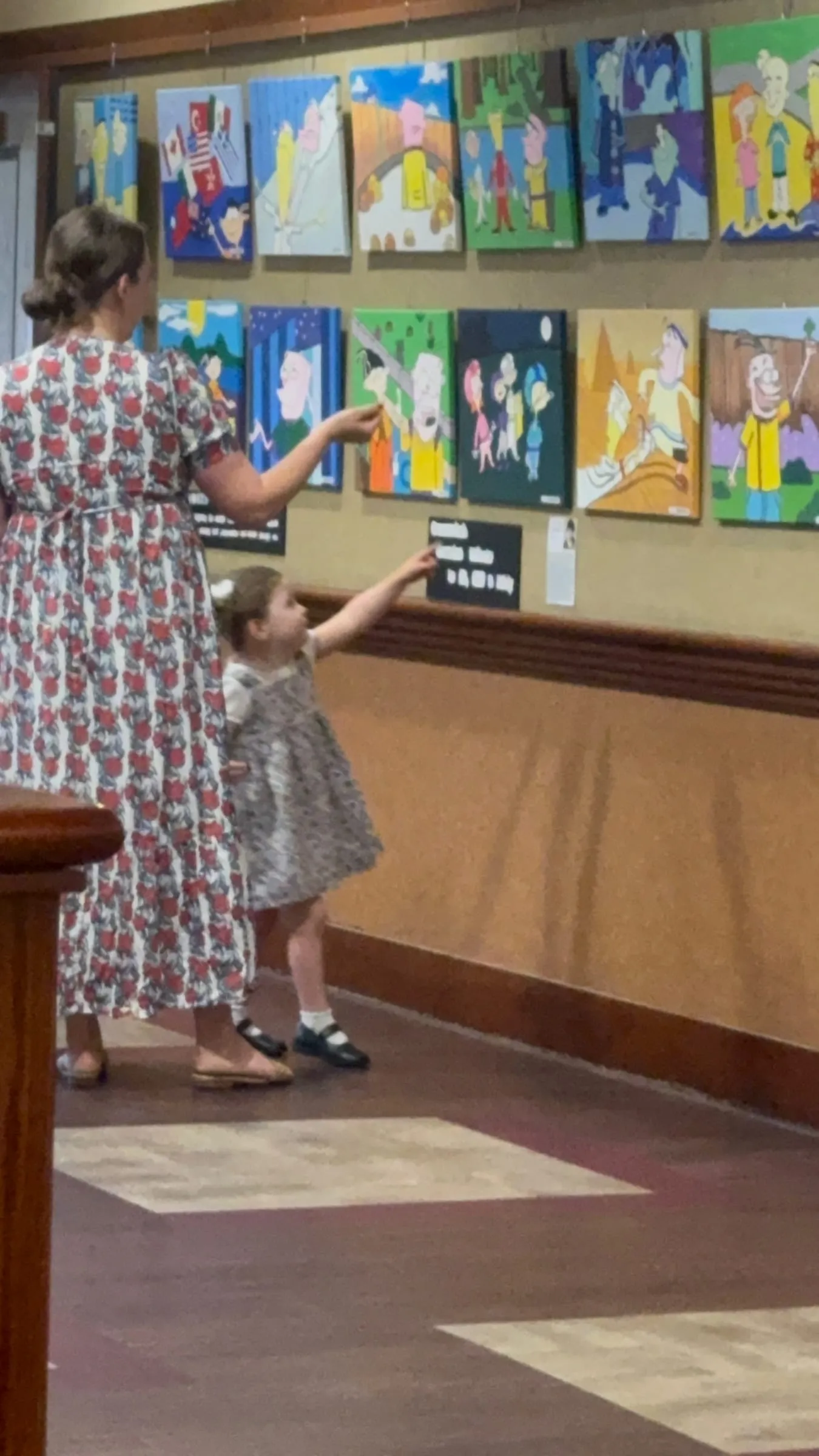 A mother and her toddler point at a row of colorful paintings at the exhibition.