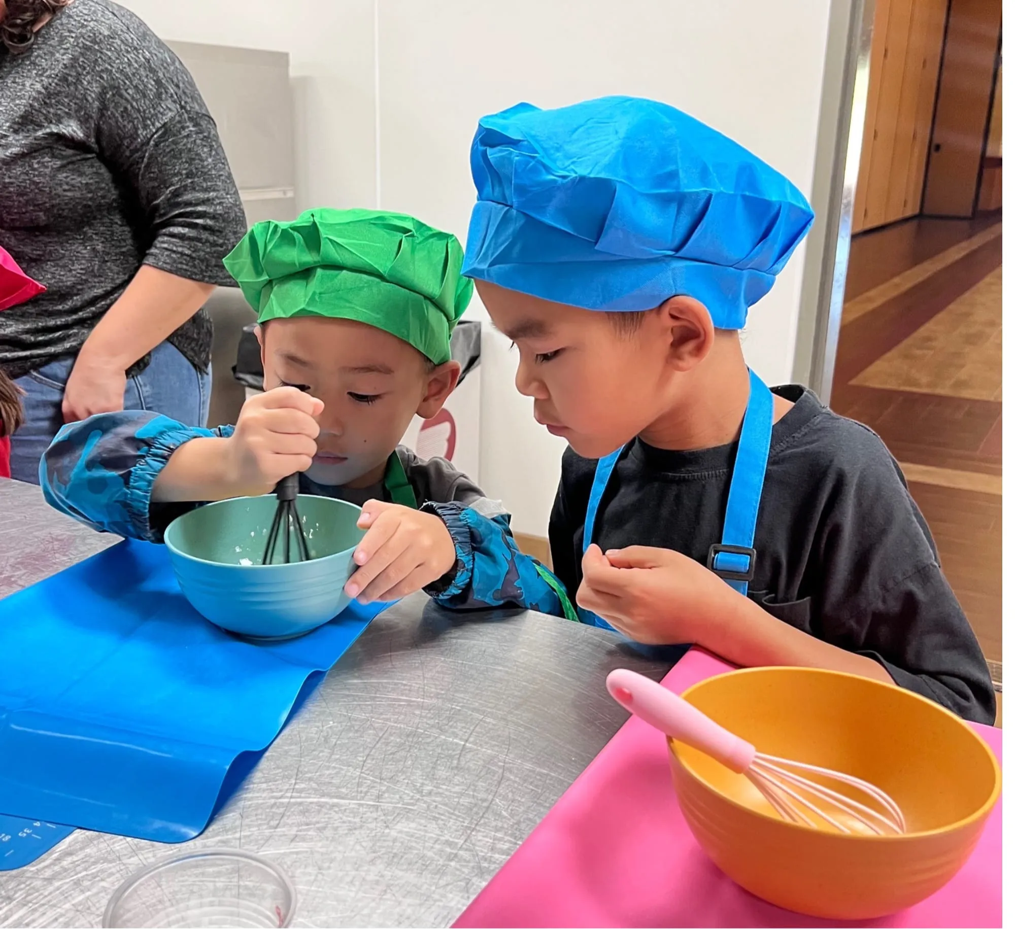 Two children in chef’s hats whisk batter together at a cooking class.